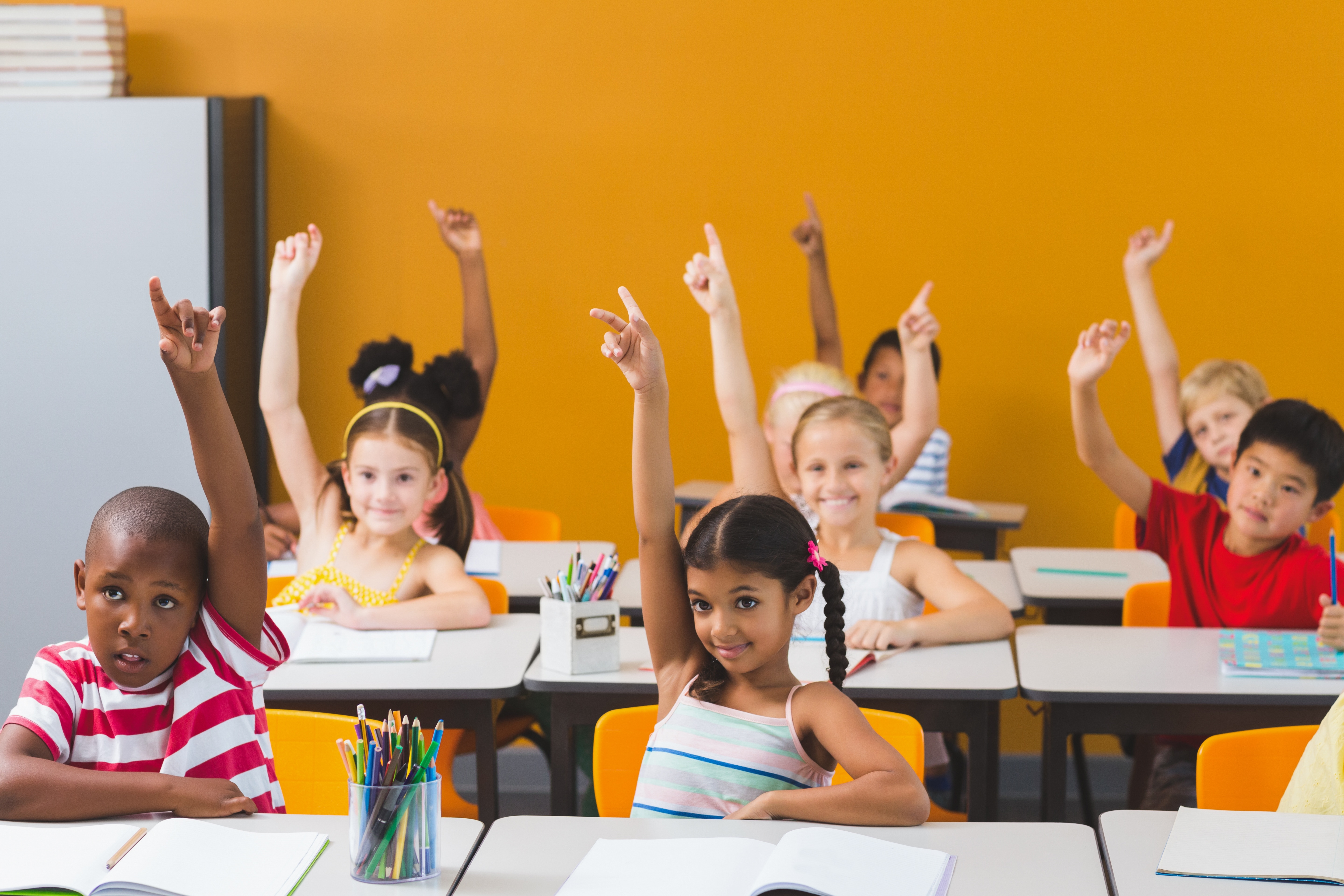 School kids raising hand in classroom.